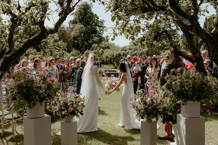 rows of wedding guests and two brides during outdoor wedding ceremony in walled garden at Byre At Inchyra 
