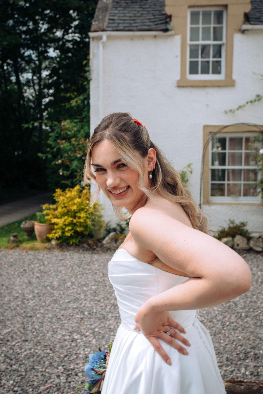 portrait shot of bride in strapless white wedding dress smiling, looking over her shoulder, with her hand placed on one hip