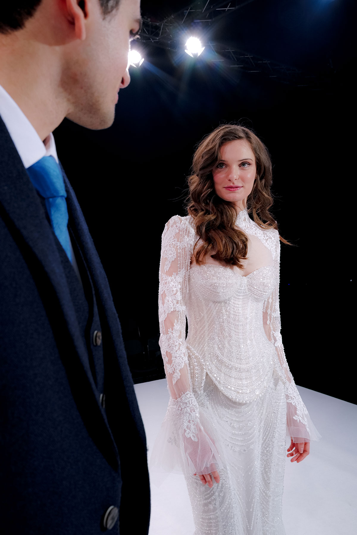 Bride in an embellished lace wedding dress looking towards a groom during a catwalk show at The Scottish Wedding Show.