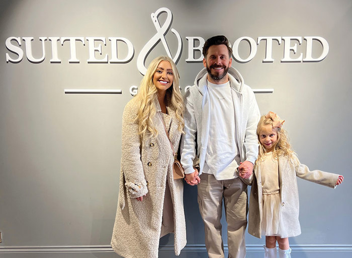 Woman in cream jacket smiling next to man in cream outfit with little girl in white oufit