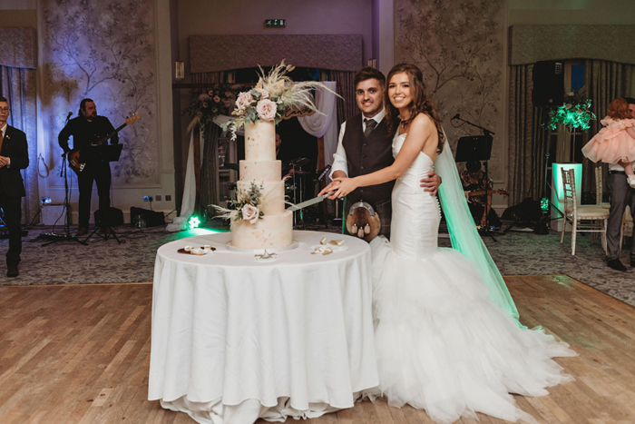 Couple smile as they cut their four-tier wedding cake