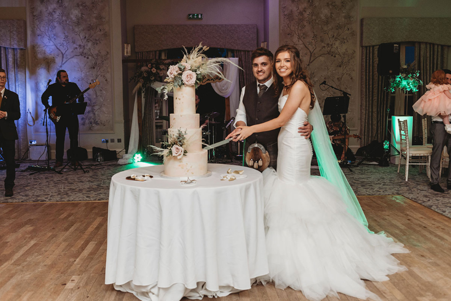 Couple smile as they cut their four-tier wedding cake