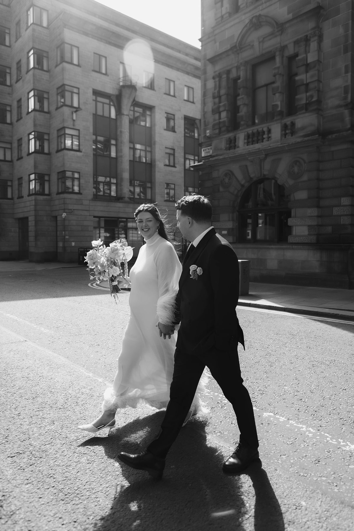 Black and white Glasgow wedding photo of bride and groom walking through the city