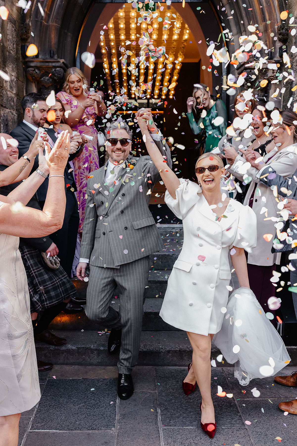 Bride and groom walk through a flurry of colourful confetti outside Virgin Hotels Edinburgh, celebrating after their Edinburgh City Chambers registry office ceremony.