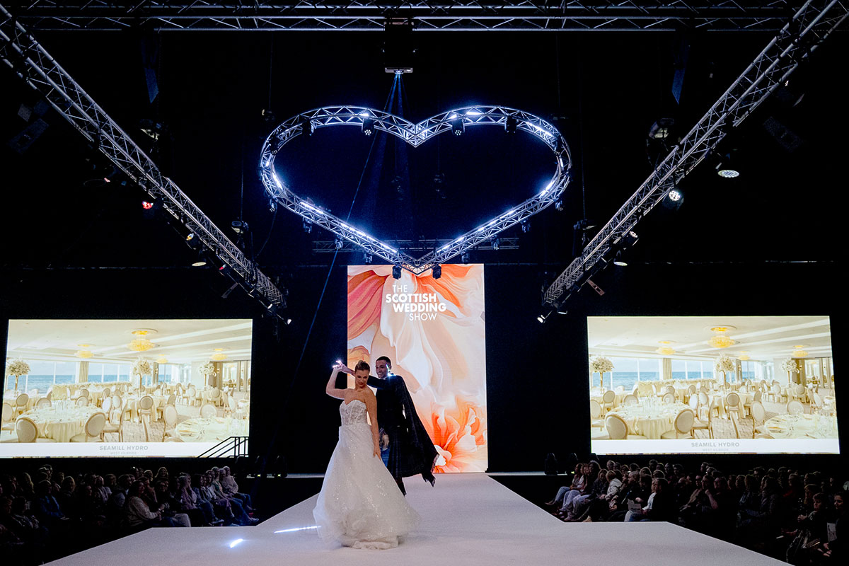 Bride and groom dancing on the RAD Runway beneath heart-shaped lighting at The Scottish Wedding Show.