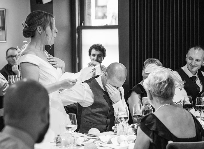 A black and white photo of a bride giving a speech in front of guests