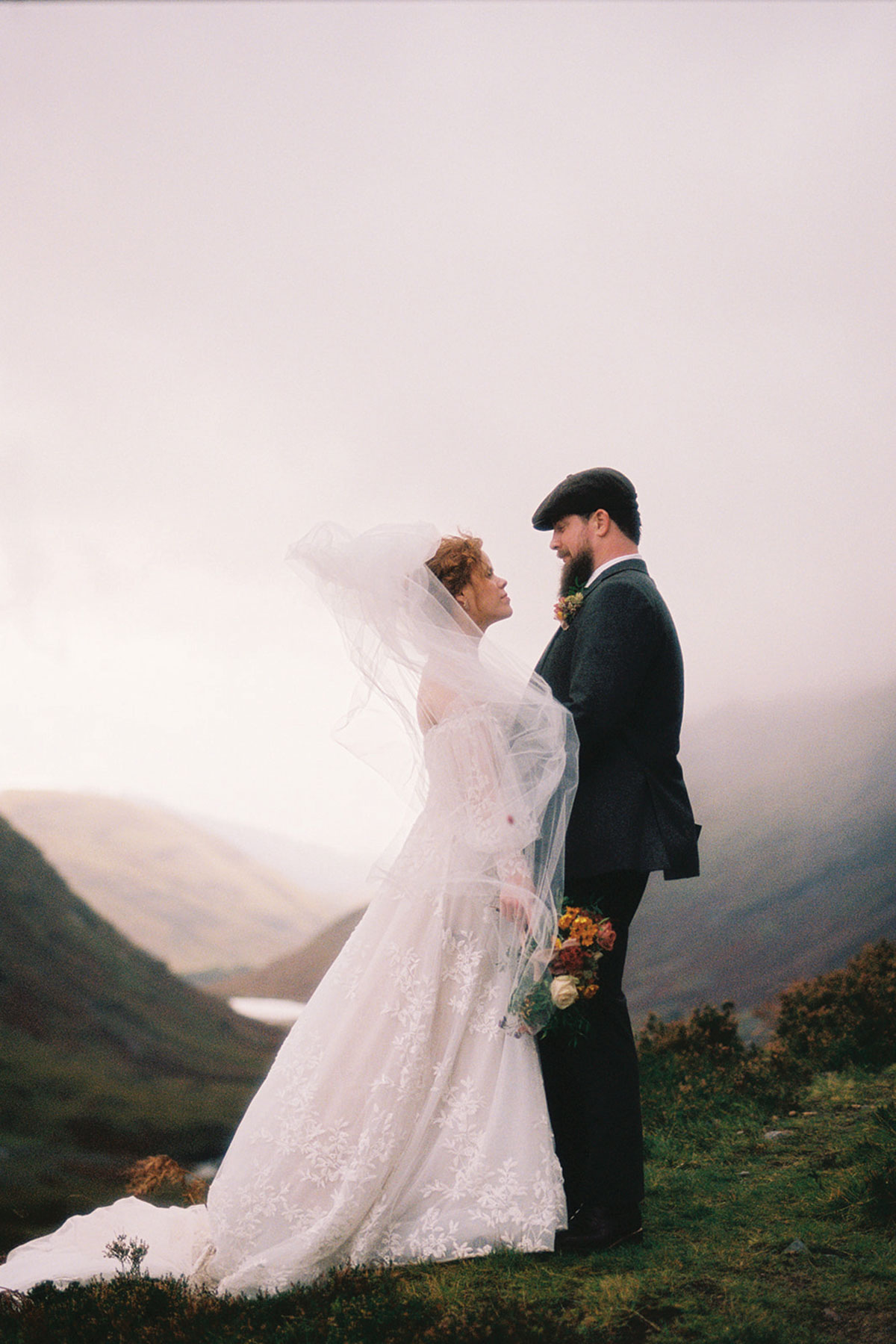 bride and groom look at one another in the scottish highlands with rain in the background