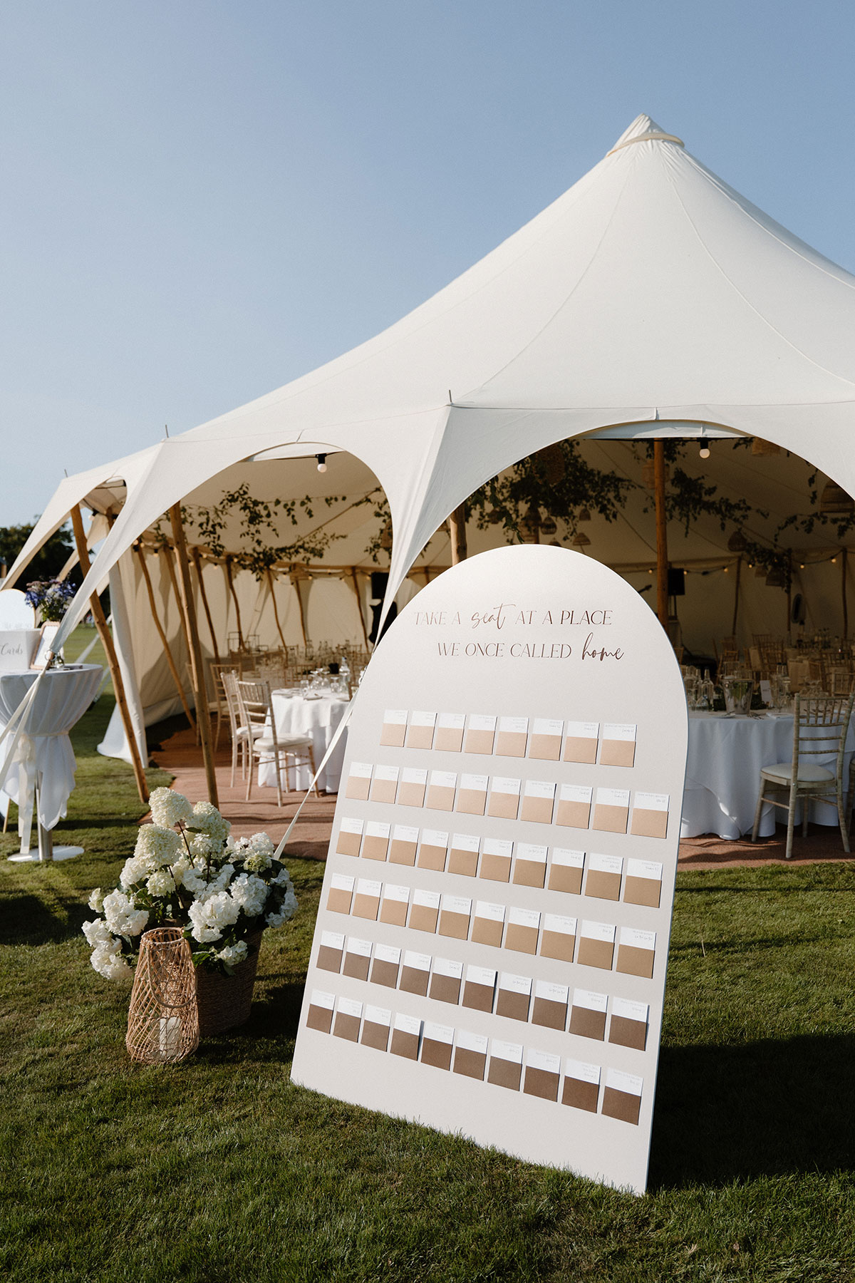 Elegant wedding seating plan displayed outside a sailcloth marquee with white florals and neutral wedding styling