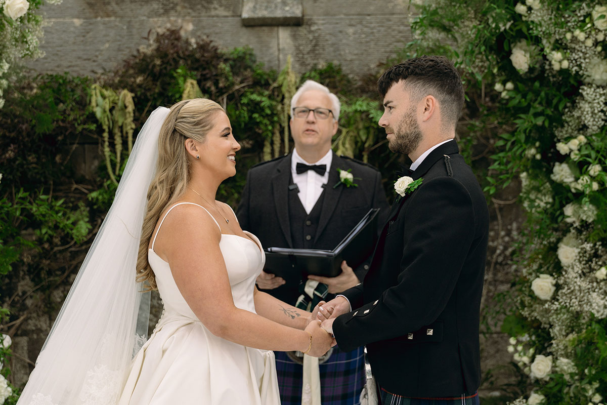 Bride and groom hold hands during romantic Scottish castle wedding ceremony in Dundas Castle courtyard.