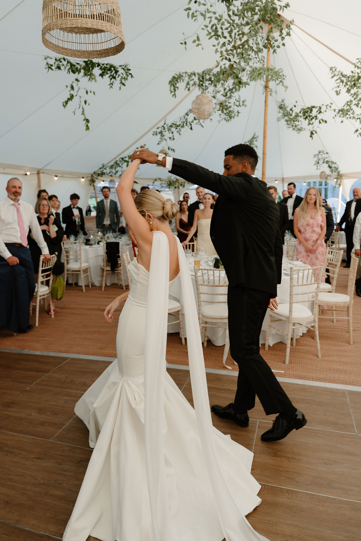 Bride and groom dancing together inside a sailcloth wedding marquee surrounded by guests and greenery décor