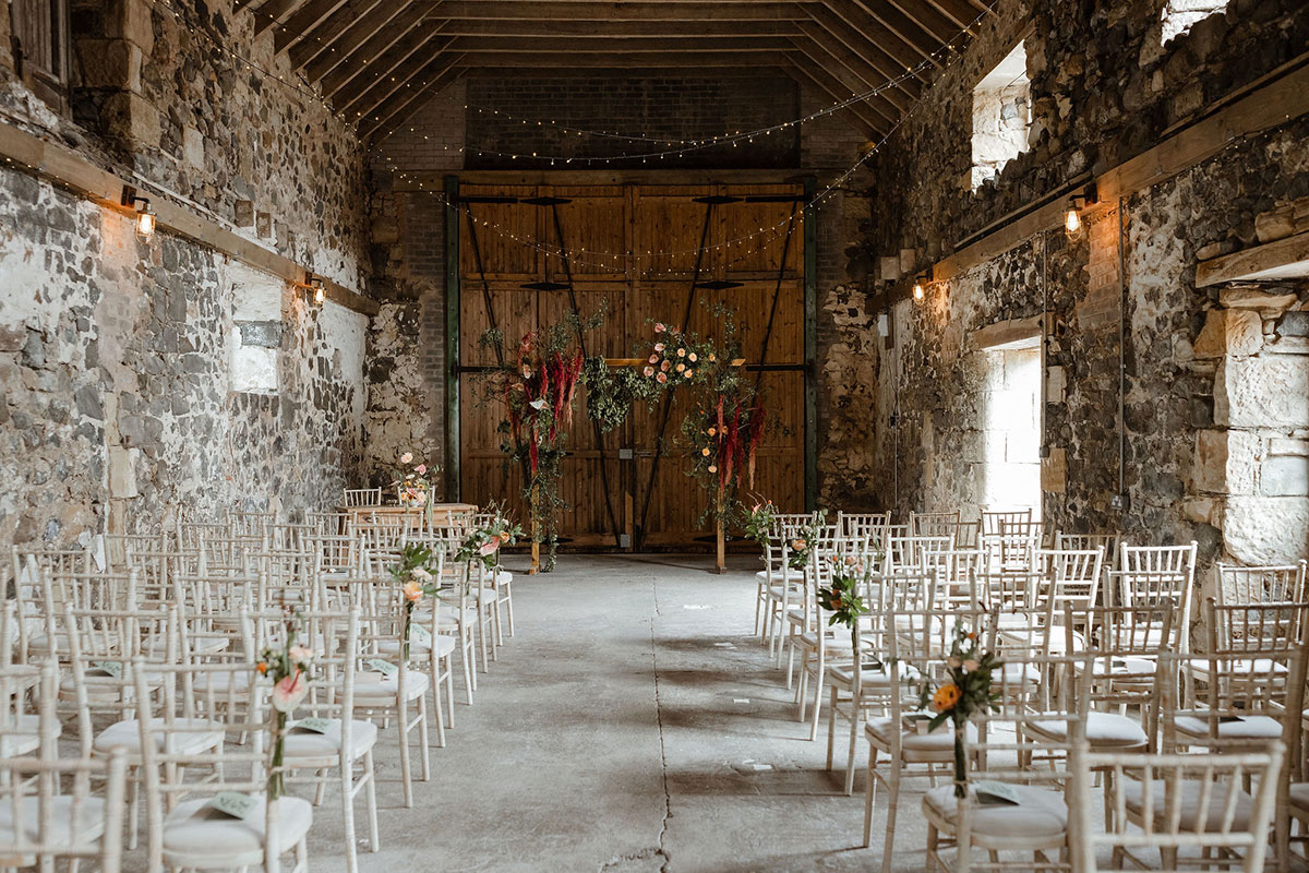 Rustic barn ceremony setup at Pratis Barns in Fife with wooden beams, stone walls and aisle seating for a Scottish wedding.