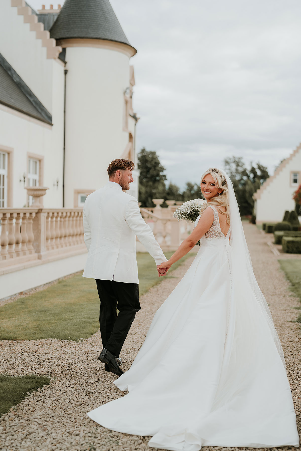 Bride and groom walking through Ingliston Country Club grounds with flowing veil