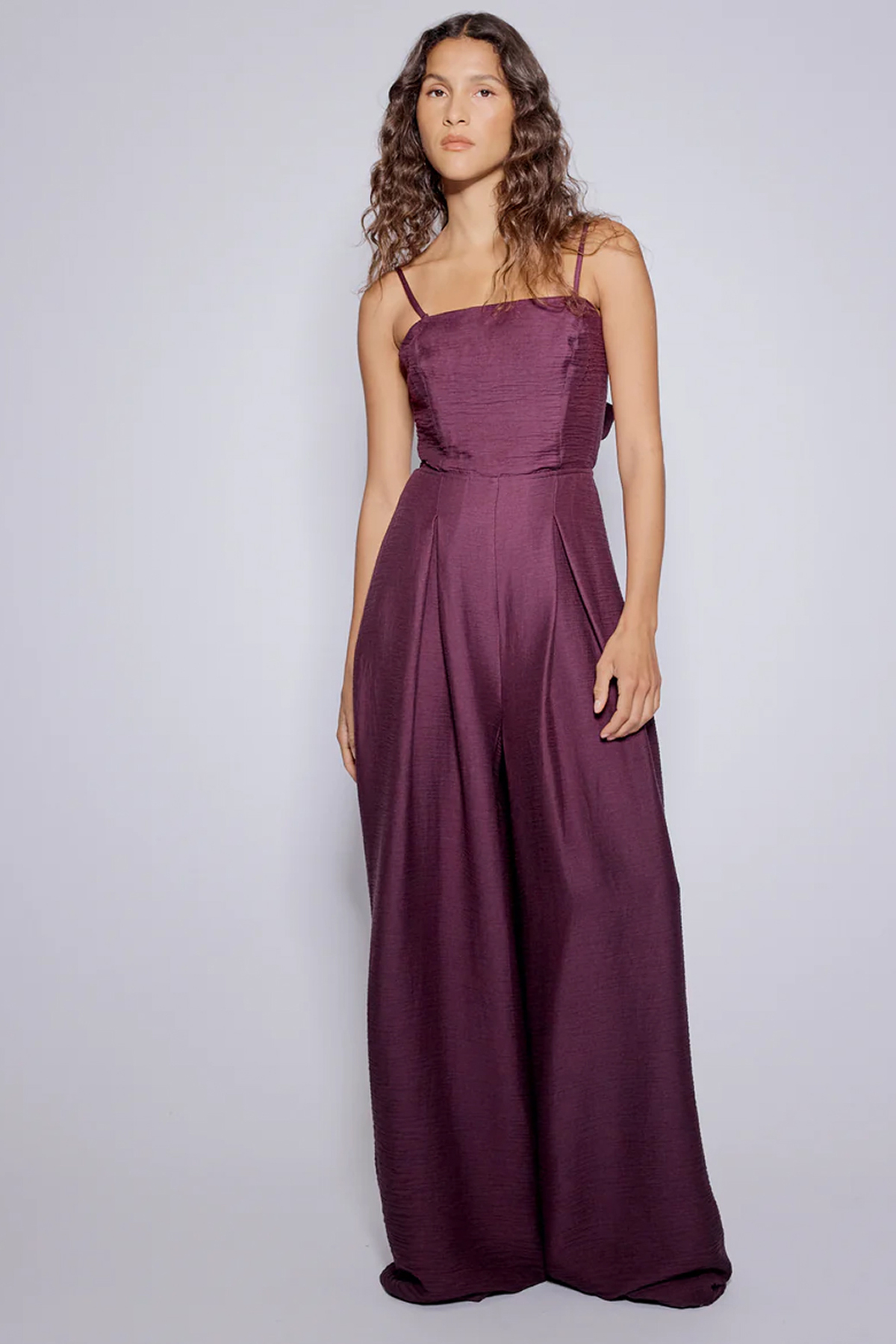 Model wearing a purple wide-leg jumpsuit with thin straps, a fitted bodice and pleated trousers.