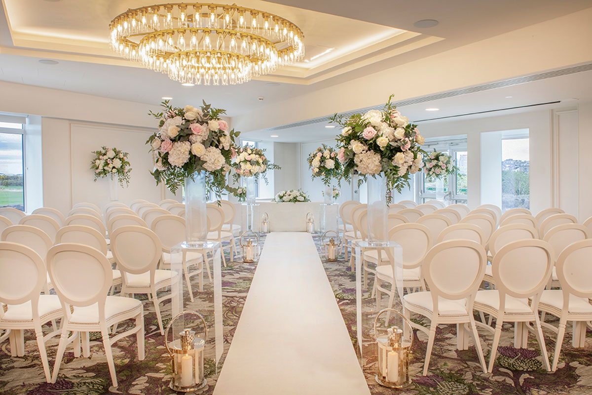 Bright modern wedding ceremony room with white chairs, floral centrepieces and contemporary chandelier lighting