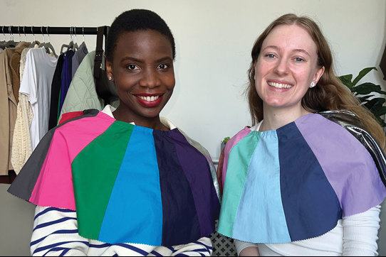 two women sit side by side with differently coloured fabric draped across their shoulders for comparison 