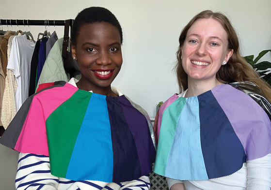 two women sit side by side with differently coloured fabric draped across their shoulders for comparison 