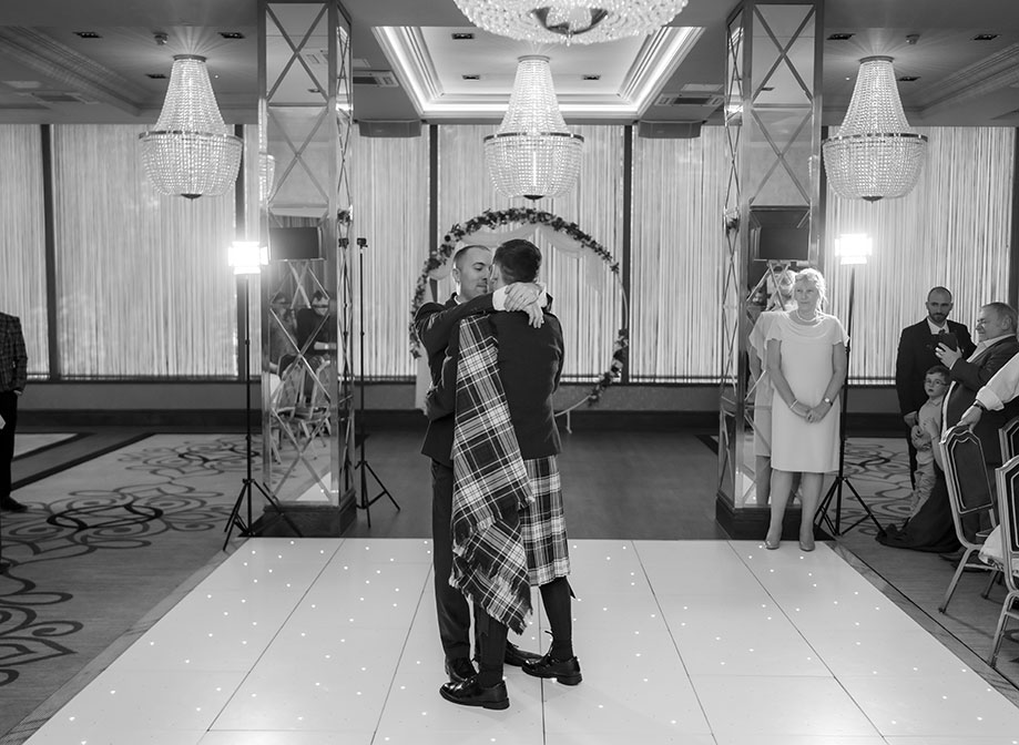 two grooms hugging while doing a first dance on a light-up dance floor