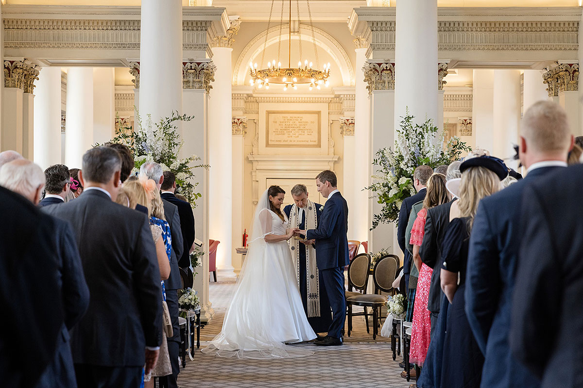 Couple exchange vows during a wedding ceremony surrounded by towering white columns in The Signet Library, Edinburgh.