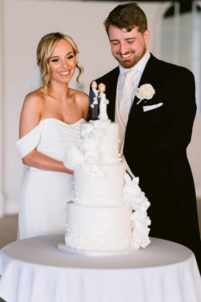 A smiling bride and groom standing next to a cake.