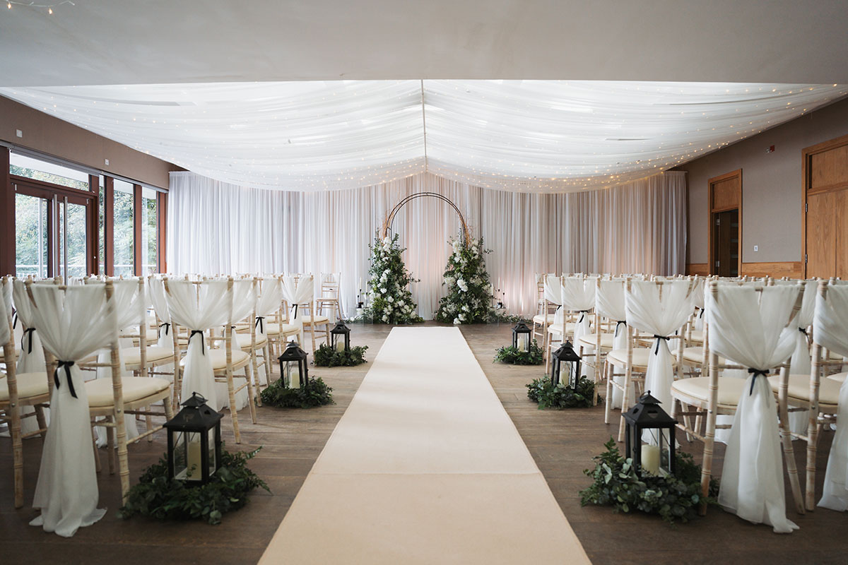 Lodge on Loch Lomond ceremony room with aisle, lanterns and floral backdrop setup