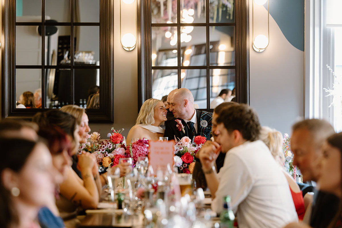Bride and groom seated together during their wedding dinner at Glaschu Restaurant & Bar in Glasgow, surrounded by guests and colourful flowers.