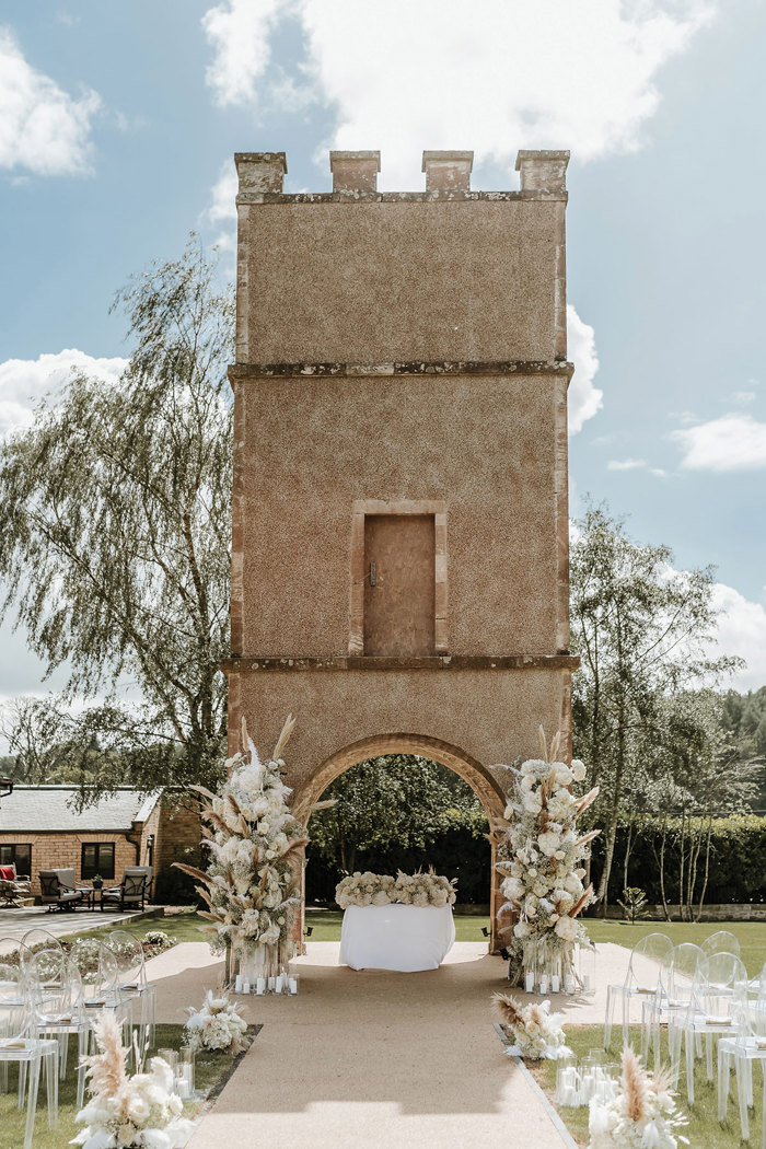 outdoor ceremony space under a single castle tower complete with an aisle lined with candles and white floral arrangements