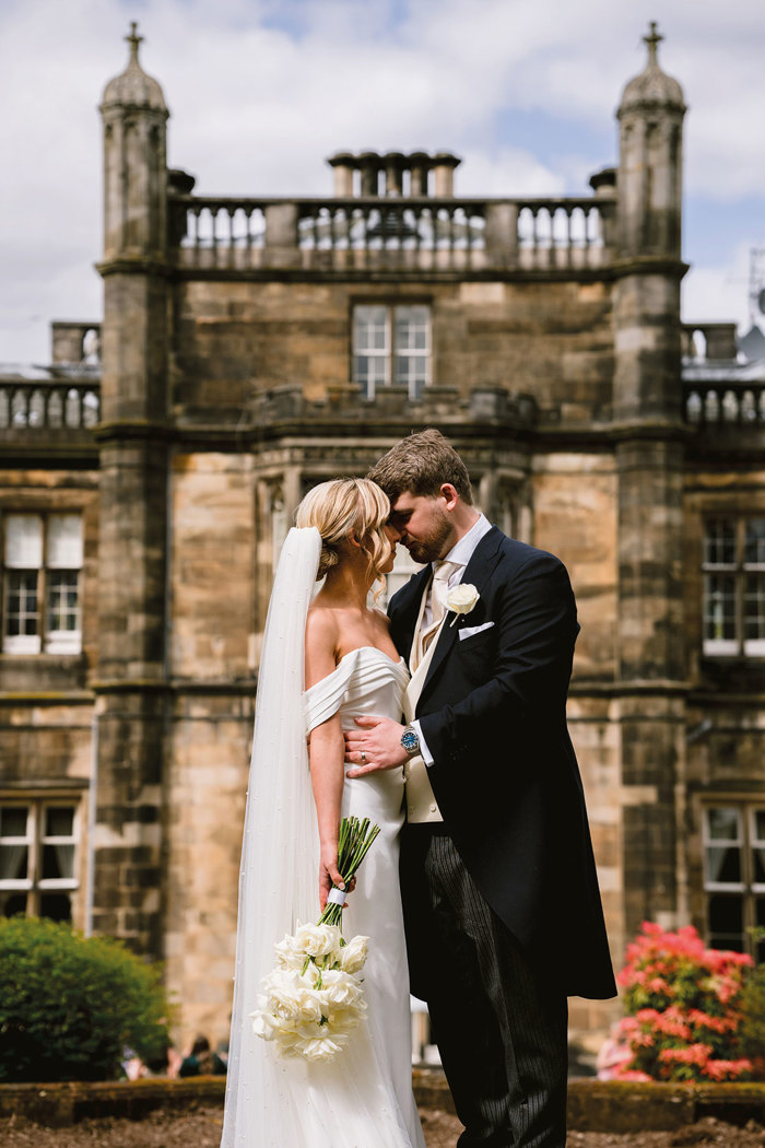 A bride and groom kissing in front of the exterior of Mar Hall.