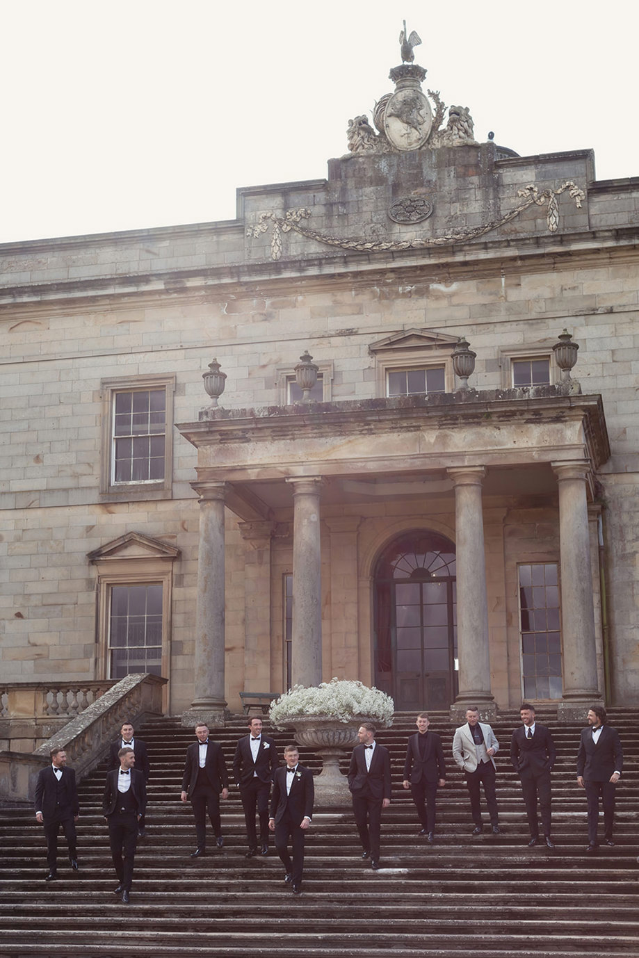 A group of men in tuxedos standing on steps in front of a stone building.