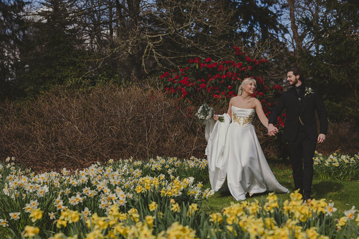 a bride and groom walking on a garden amid daffodils.