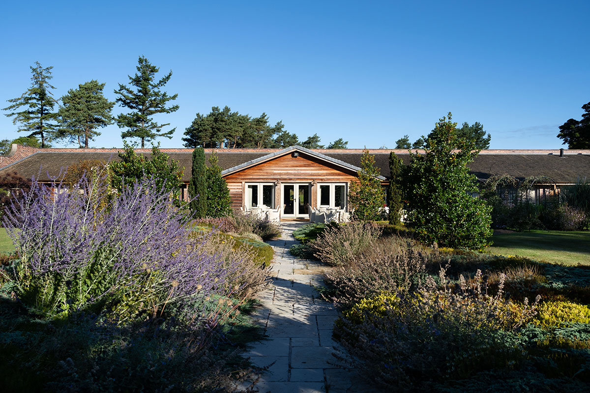 exterior image of a single storey cottage with a grey stone path surrounded by lavender and other greenery leading up to the french doors