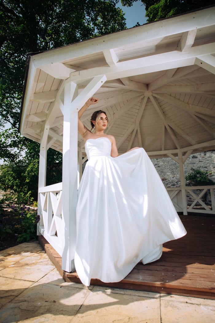 upward angled image of a bride in strapless wedding dress standing in the opening of a gazebo with her one arm in the air