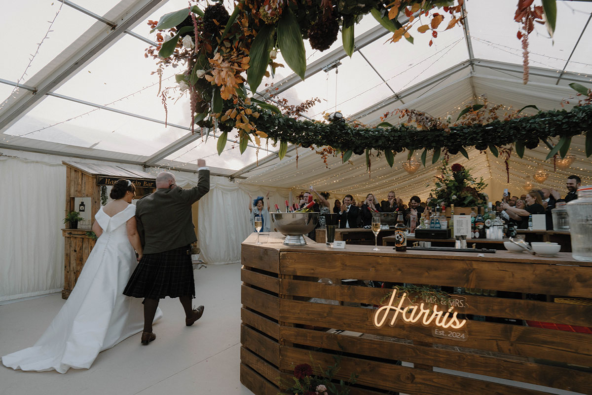 Bride and groom entering the wedding marquee at Cluny Castle as guests cheer during their autumn reception.
