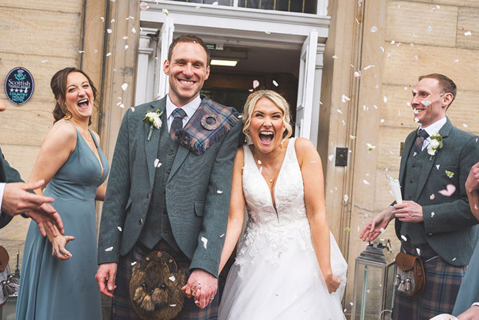 bride and groom hold hands and smile from ear to ear during their confetti toss