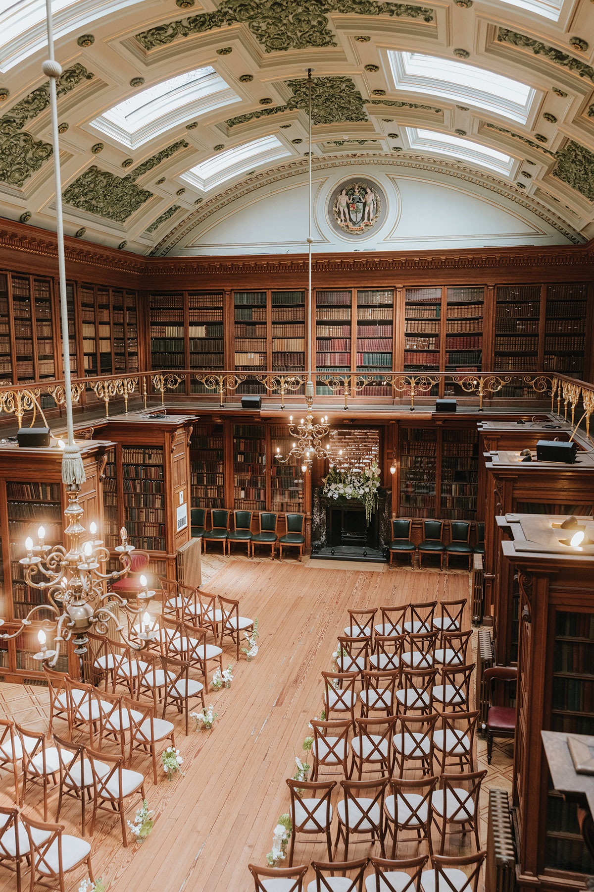 Historic library wedding ceremony setup with wooden chairs, chandeliers, and ornate bookshelves