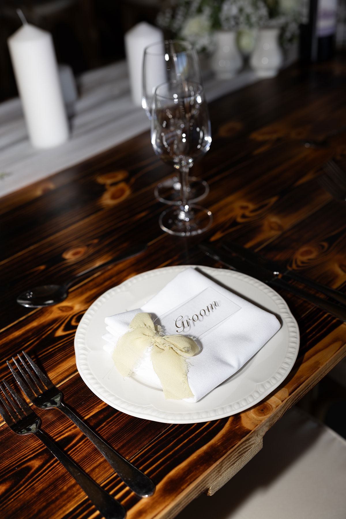 A table at a Falside Mill barn wedding set with a white plate and a perspex 'groom' place setting and bow on the napkin
