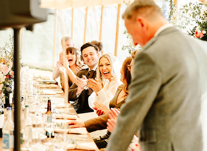 a row of people sitting at a top table clapping as a person stands making a speech