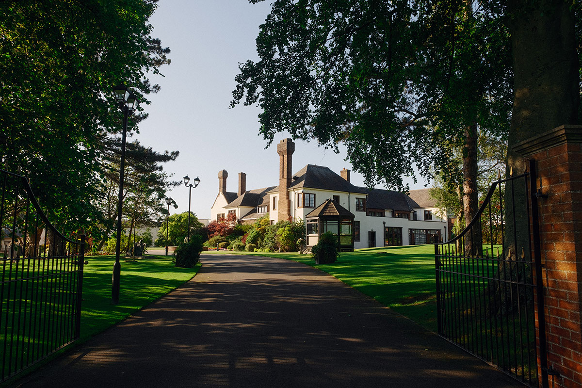 Driveway entrance leading to the white manor-style exterior of Western House Hotel, surrounded by trees and lawns.