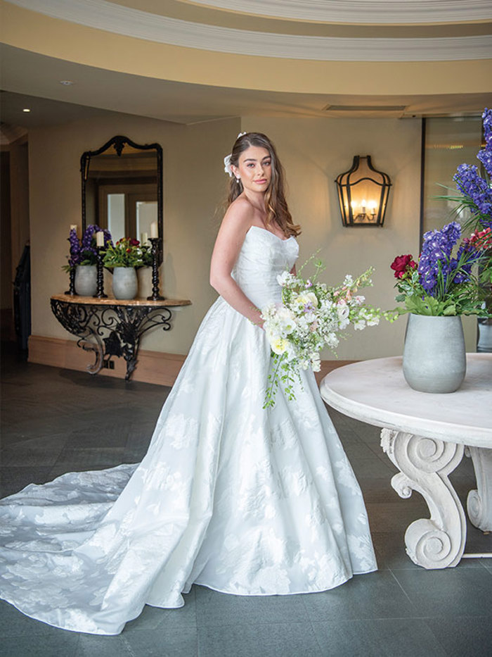 A woman wearing a long wedding dress with a train holding a white bouquet