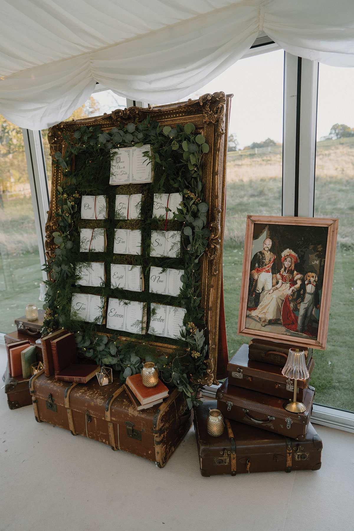 Gold-framed table plan decorated with foliage and vintage suitcases at Cluny Castle wedding reception.