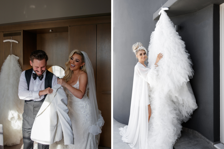 Bride in white dress smiling helping groom put white jacket on, with bride standing in white robe looking at white dress with train hanging up