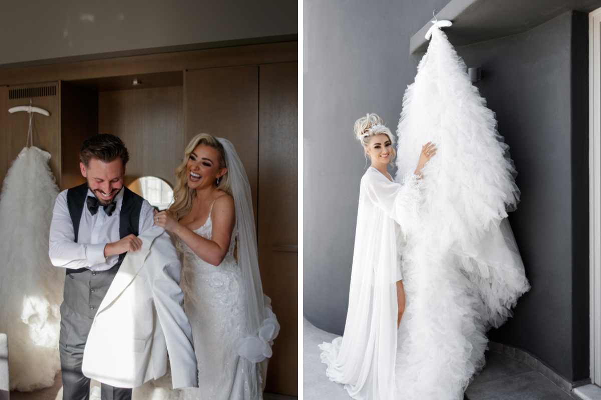 Bride in white dress smiling helping groom put white jacket on, with bride standing in white robe looking at white dress with train hanging up