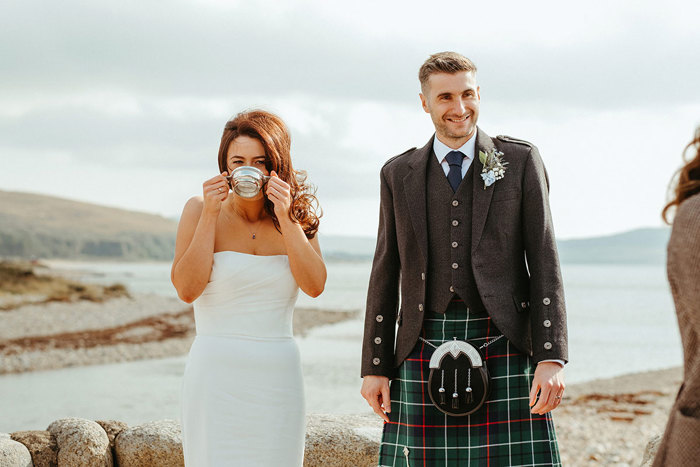 bride drinks from quiach as groom stands next to her