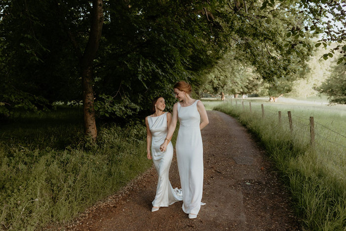 two brides walking hand in hand along a path under trees at Byre At Inchyra 