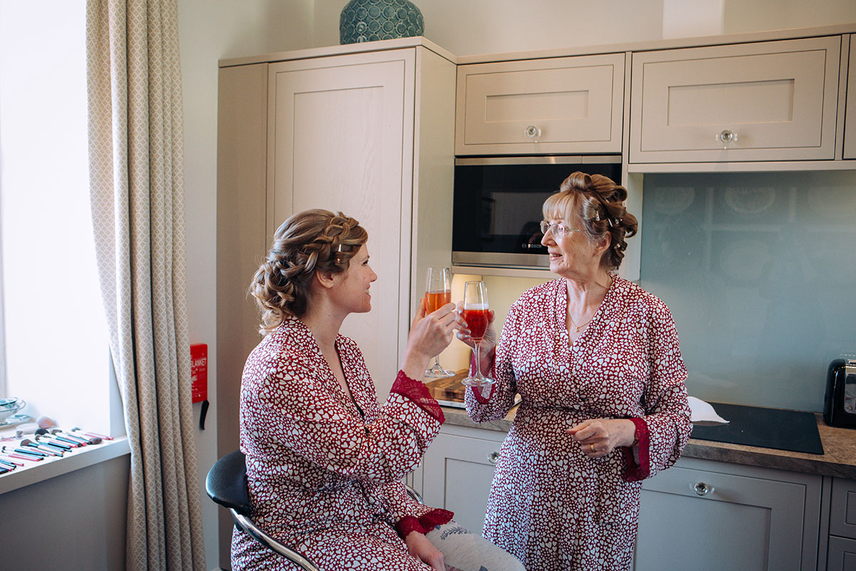 Bride and her mother toasting glasses, wearing red and white love heart print dressing gowns