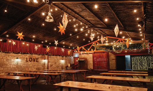 inside view of a barn filled with rows of wooden table and twinkly star lanterns from ceiling