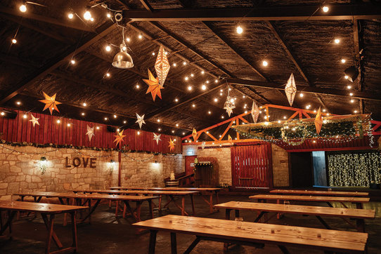 inside view of a barn filled with rows of wooden table and twinkly star lanterns from ceiling