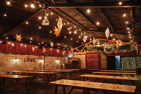 inside view of a barn filled with rows of wooden table and twinkly star lanterns from ceiling