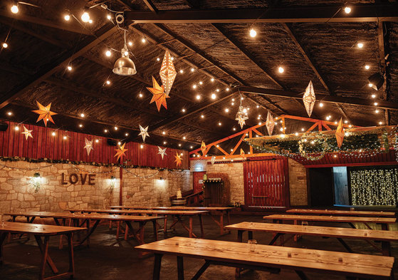 inside view of a barn filled with rows of wooden table and twinkly star lanterns from ceiling