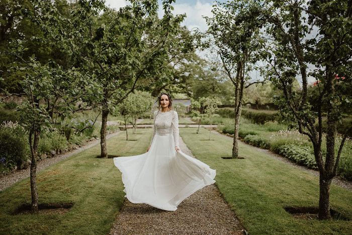 Bride swishes skirt of wedding dress in garden