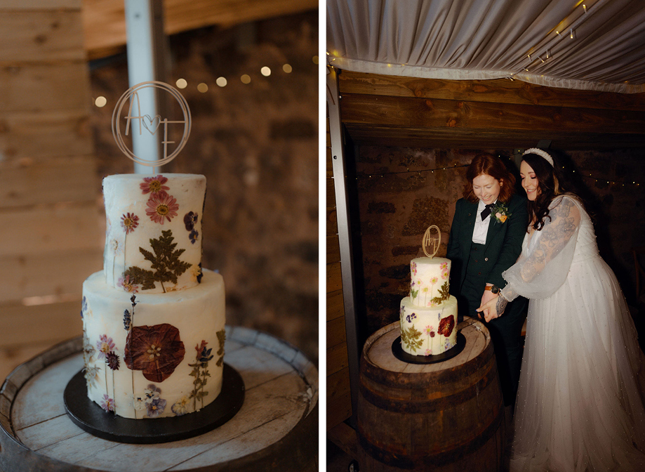 a two tier wedding cake decorated with pressed dried flowers sitting on a wooden barrel on left. Two brides cutting the wedding cake on right.